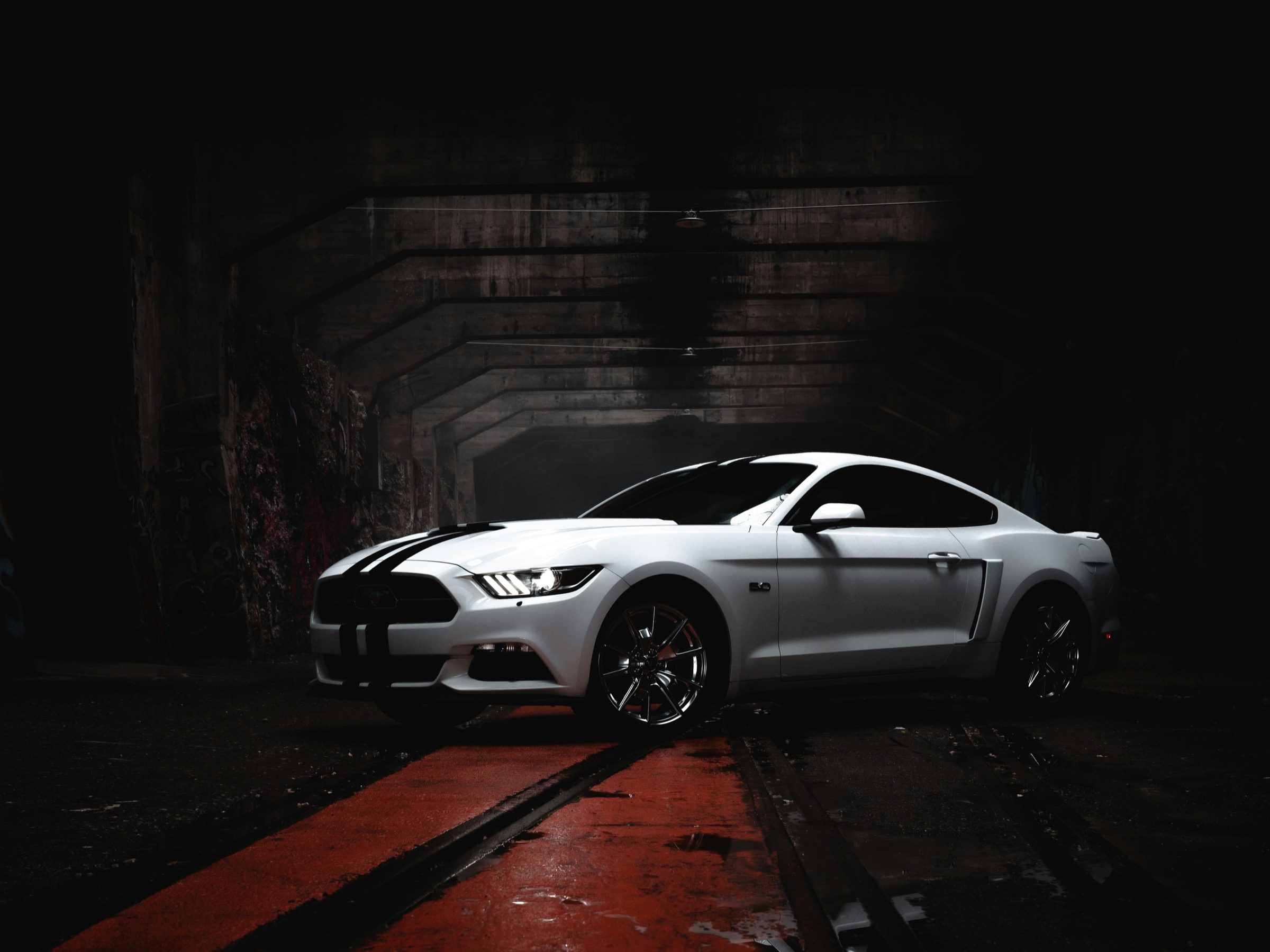 White Ford Mustang with racing stripes in a dark warehouse